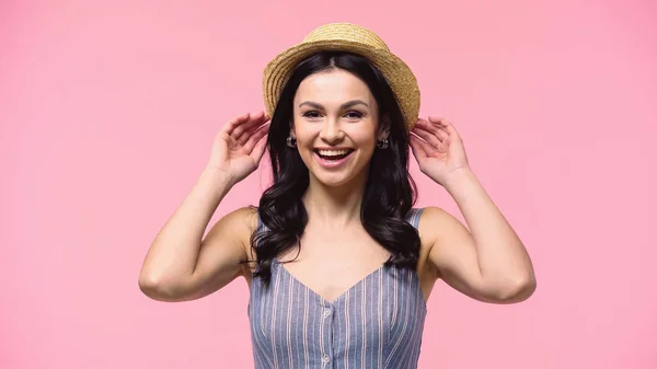 Mujer feliz ajustando sombrero de paja aislado en rosa - foto de stock