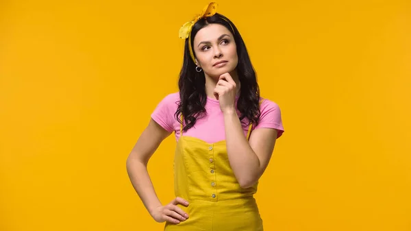 Femme pensive tenant la main sur la hanche isolée sur jaune — Photo de stock
