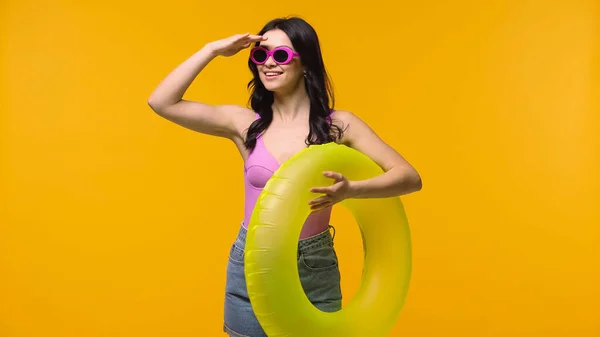Усміхнена жінка з плавальним кільцем дивиться ізольовано на жовтому — стокове фото