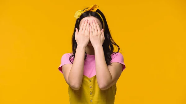 Молода жінка прикриває обличчя відьмами руки ізольовані на жовтому — стокове фото