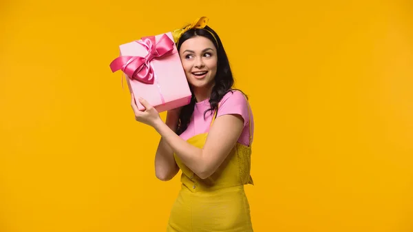 Mujer positiva sosteniendo presente cerca de la oreja aislada en amarillo - foto de stock