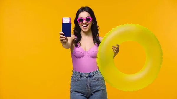 Excited woman showing passport while holding swim ring isolated on yellow — Stock Photo