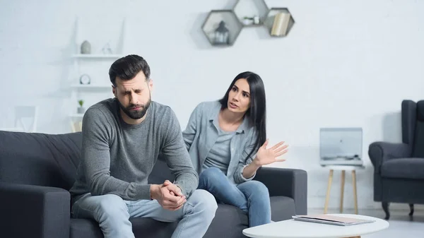 Mujer disgustada hablando cerca del hombre con los ojos cerrados en la sala de estar — Stock Photo