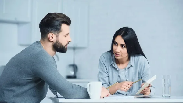 Woman holding calculator and taking with upset man at home — Stock Photo