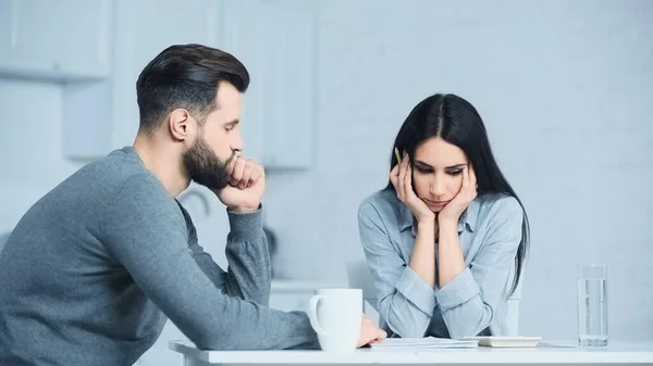 Femme triste regardant la calculatrice tout en étant assis avec l'homme contrarié à la maison — Photo de stock