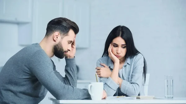 Frustrierte Frau blickt auf Taschenrechner und pustet Wangen bei aufgebrachtem Mann zu Hause — Stockfoto