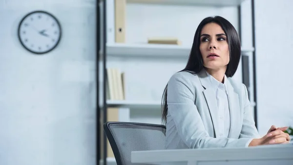 Mujer de negocios preocupada mirando hacia otro lado mientras está sentada en el escritorio - foto de stock