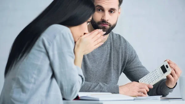Upset man showing calculator to blurred and sad woman — Stock Photo