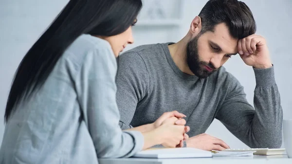 Molesto hombre mirando calculadora cerca borrosa triste mujer - foto de stock