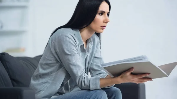 Verärgerte Frau hält Ordner in der Hand und sitzt zu Hause auf Sofa — Stockfoto