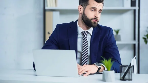 Homem de negócios chateado em terno olhando para longe perto do laptop na mesa — Fotografia de Stock