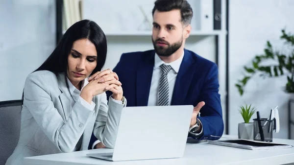 Sad businesswoman looking away near blurred businessman quarrelling in office — Stock Photo