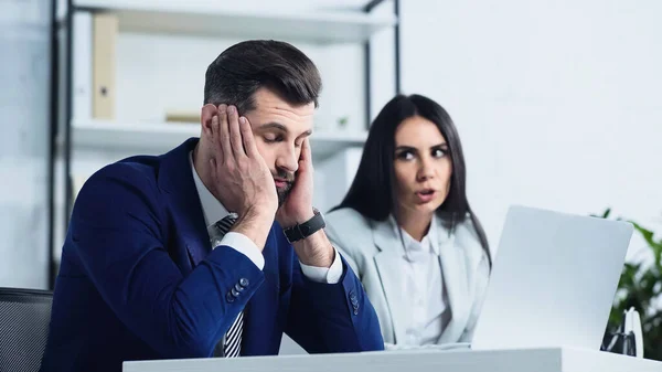 Расстроенный бизнесмен с закрытыми глазами рядом размытые деловые женщины ссорятся в офисе — стоковое фото
