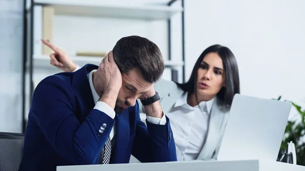 Frustrated businessman near blurred businesswoman pointing with finger while quarrelling in office — Stock Photo