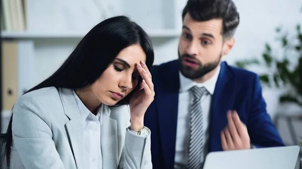 Triste mujer de negocios con dolor de cabeza cerca borrosa y discutiendo hombre de negocios - foto de stock