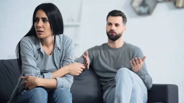 Mujer frustrada sentada cerca borrosa y disgustado novio peleando en la sala de estar - foto de stock