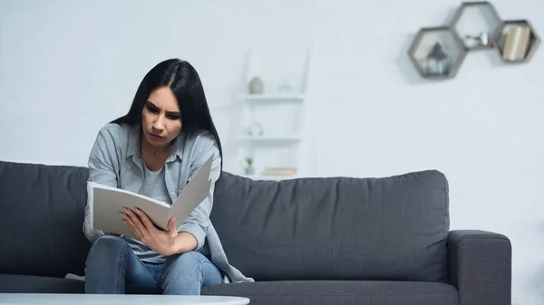 Mujer preocupada mirando la carpeta con documentos en la sala de estar - foto de stock