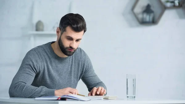 Unzufriedener Mann blickt auf Notizbuch neben Taschenrechner auf Tisch — Stockfoto