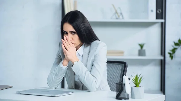 Femme inquiète avec les mains serrées assis près de l'ordinateur portable sur le bureau — Photo de stock