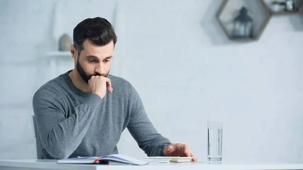 Displeased man looking at notebook with accounting near calculator on table — Stock Photo