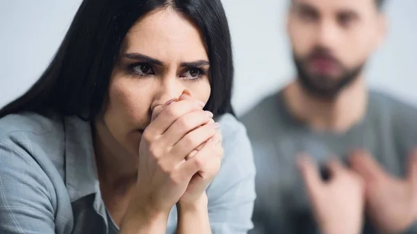 Morena mujer con las manos cerradas cubriendo la cara cerca de hombre borroso - foto de stock