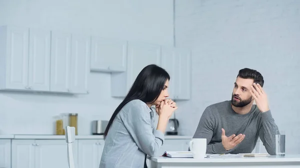 Homem gesticulando ao discutir finanças com a mulher na cozinha — Fotografia de Stock