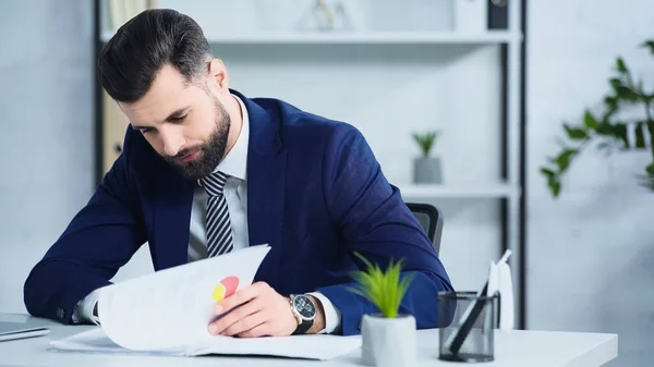 Hombre de negocios deprimido en traje mirando documentos en la oficina - foto de stock