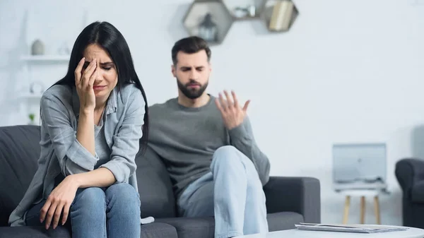 Aufgebrachte Frau weint in der Nähe eines unscharfen und unzufriedenen Freundes, der sich zu Hause streitet — Stockfoto