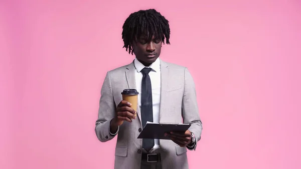 African american businessman with clipboard holding coffee isolated on pink — Stock Photo