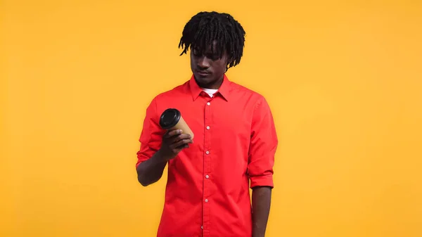 Junger afrikanisch-amerikanischer Mann blickt auf Pappbecher mit Kaffee isoliert auf gelb — Stockfoto