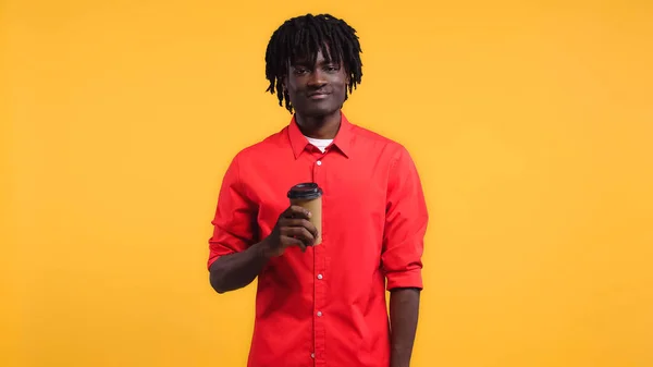 Heureux homme afro-américain tenant du café pour aller dans une tasse en papier isolé sur jaune — Photo de stock