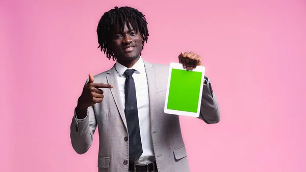 Cheerful african american businessman pointing at digital tablet isolated on pink — Stock Photo