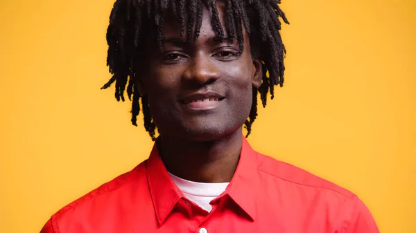 Hombre afroamericano feliz en camisa roja sonriendo aislado en amarillo - foto de stock