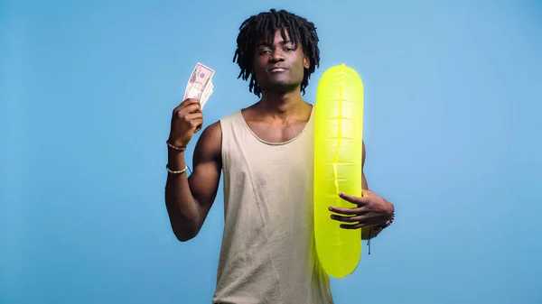 Hombre afroamericano con anillo inflable ondeando dinero aislado en azul - foto de stock