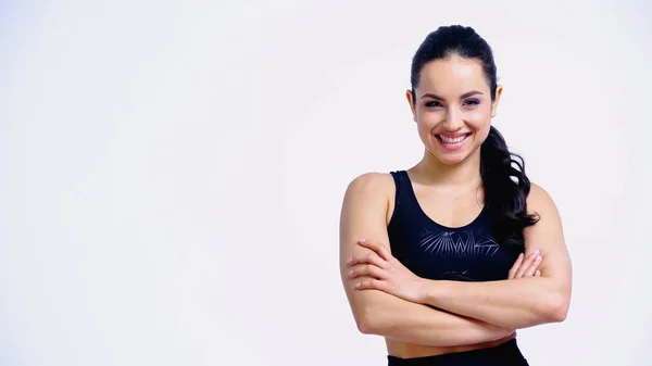 Feliz jovem mulher em sportswear de pé com os braços cruzados e olhando para a câmera isolada no branco — Fotografia de Stock