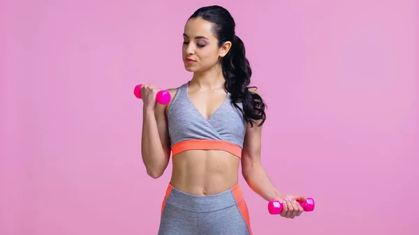 Morena deportista haciendo ejercicio con mancuernas aisladas en rosa - foto de stock