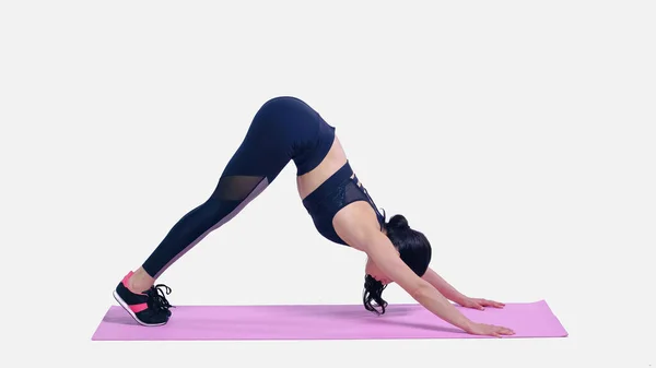 Longitud completa de la deportista estiramiento en rosa alfombra de fitness en blanco - foto de stock