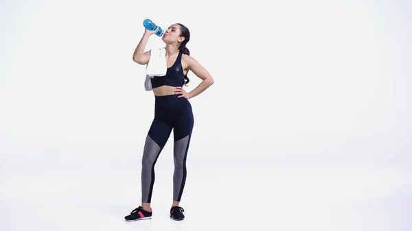 Junge Sportlerin mit Handtuch trinkt Wasser aus Sportflasche auf weiß — Stockfoto