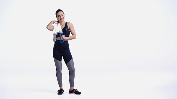 Happy sportswoman with towel and sports bottle standing on white — Stock Photo