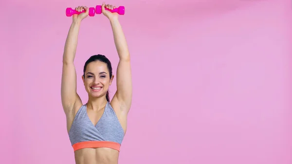 Mujer feliz haciendo ejercicio con mancuernas aisladas en rosa - foto de stock