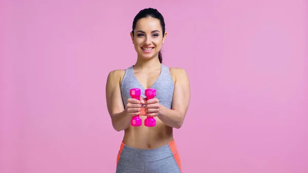 Sonriente joven haciendo ejercicio con mancuernas aisladas en rosa - foto de stock