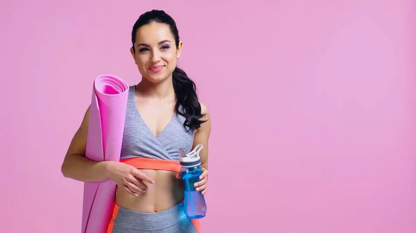 Desportista feliz segurando garrafa de esportes e tapete de fitness isolado em rosa — Fotografia de Stock