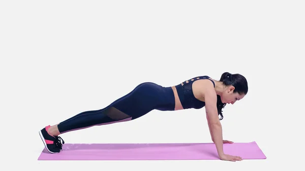 Brunette sportive faisant de l'exercice de planche sur tapis de fitness rose sur blanc — Photo de stock