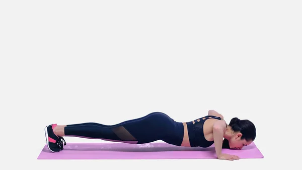 Morena joven deportista haciendo ejercicio en rosa alfombra de fitness en blanco - foto de stock