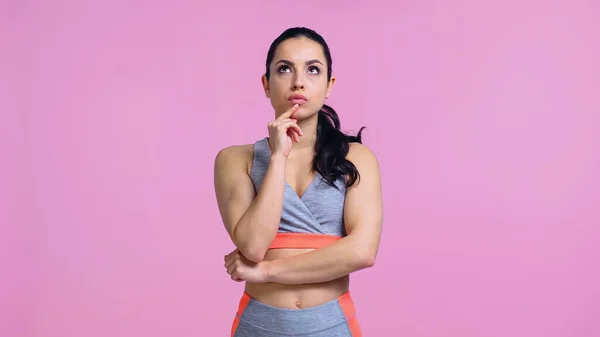 Mujer joven reflexiva en ropa deportiva mirando hacia otro lado aislado en rosa - foto de stock