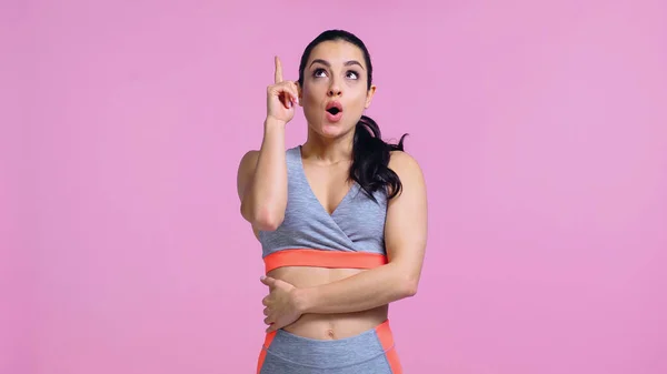 Überraschte junge Frau in Sportbekleidung zeigt mit dem Finger und blickt vereinzelt auf rosa — Stockfoto