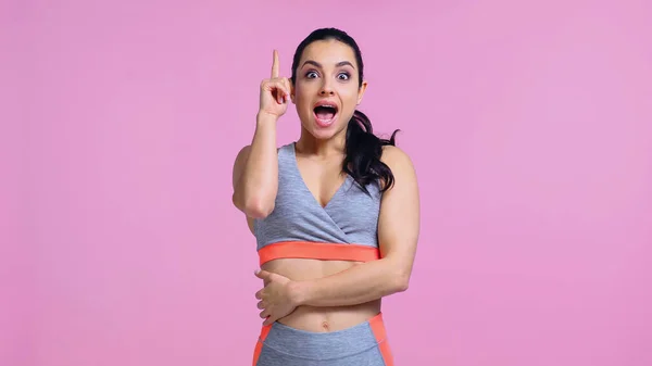 Excitada joven en ropa deportiva señalando con el dedo aislado en rosa - foto de stock