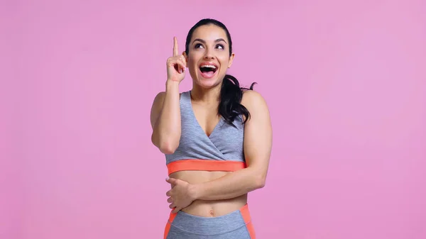 Mujer joven sorprendida en ropa deportiva señalando con el dedo y mirando hacia arriba aislado en rosa - foto de stock