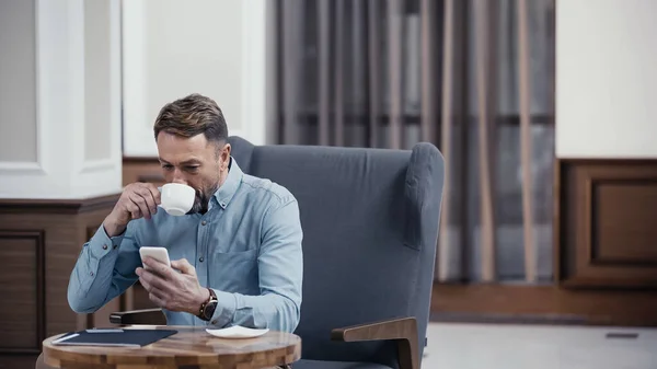 Geschäftsmann benutzt Smartphone und trinkt Kaffee in Lobby eines Restaurants — Stockfoto