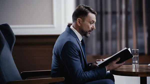 Seitenansicht des Geschäftsmannes, der eine Papiermappe mit Dokumenten hält und in der Lobby des Restaurants spricht — Stockfoto